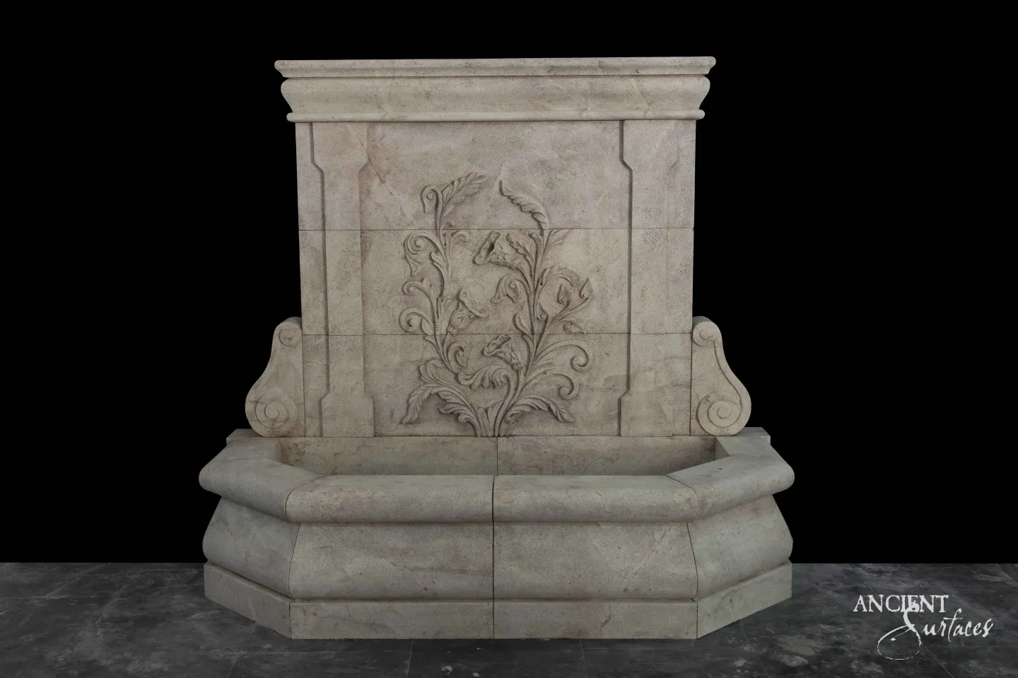 Reclaimed antique limestone wall fountain from Ancient Surfaces carved with a spray of acanthus leaves and flowers on scrolled brackets above an octagonal basin, photographed against black