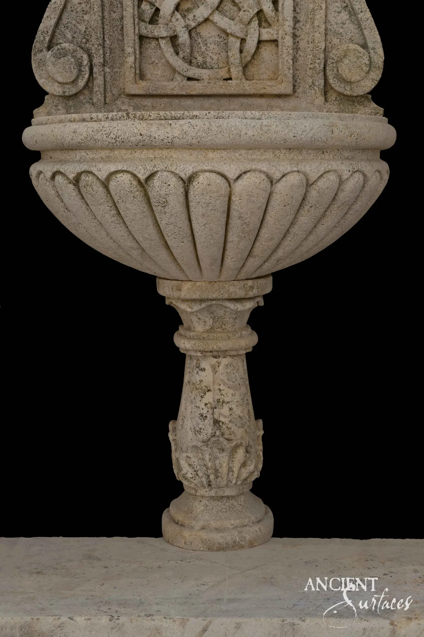 Close detail of a reclaimed antique limestone fountain bowl from Ancient Surfaces, deeply gadrooned above a carved baluster socle worked with acanthus leaves, photographed against black