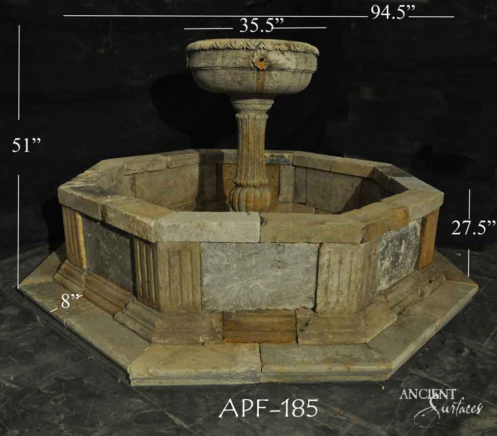 Reclaimed antique limestone fountain from Ancient Surfaces, catalogued as APF 185, with a fluted panel octagonal basin and a gadrooned urn shaped bowl on a baluster pedestal, photographed against black with dealer measurements of 94.5 inches wide
