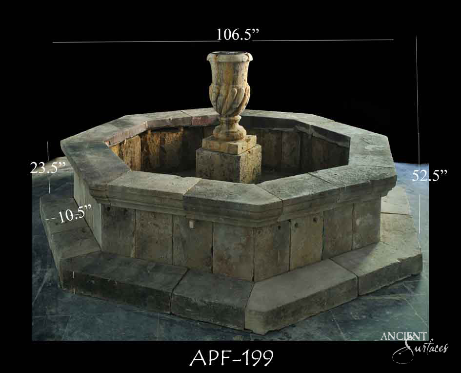 Reclaimed antique limestone fountain from Ancient Surfaces, catalogued as APF 199, with an octagonal basin built from repurposed stone blocks and a carved campana urn, photographed against black with dealer measurements of 106.5 inches wide